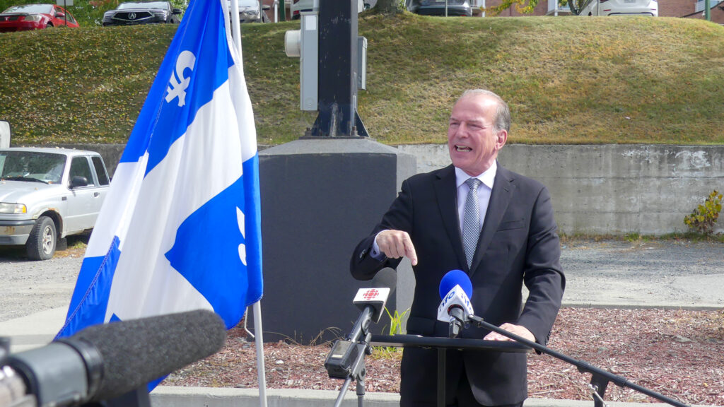 André Bachand s'adresse aux médias aux côtés d'un drapeau du Québec